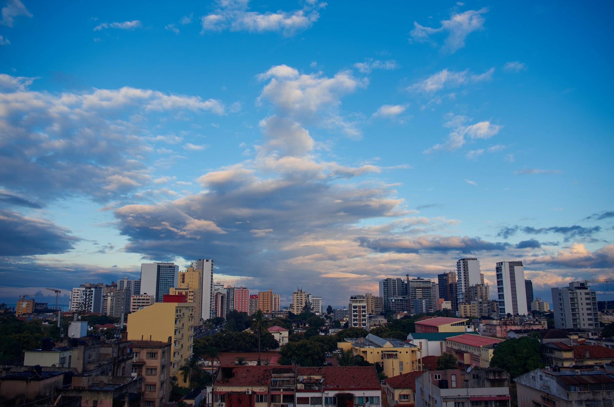 O centro de Maputo sob um céu nublado, com edifícios altos acima das árvores.